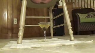 Woman squats on a chair and pisses on a martini glass